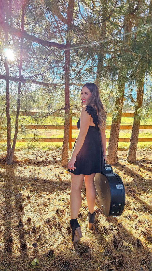Aliki carrying her guitar case through sunlit pines