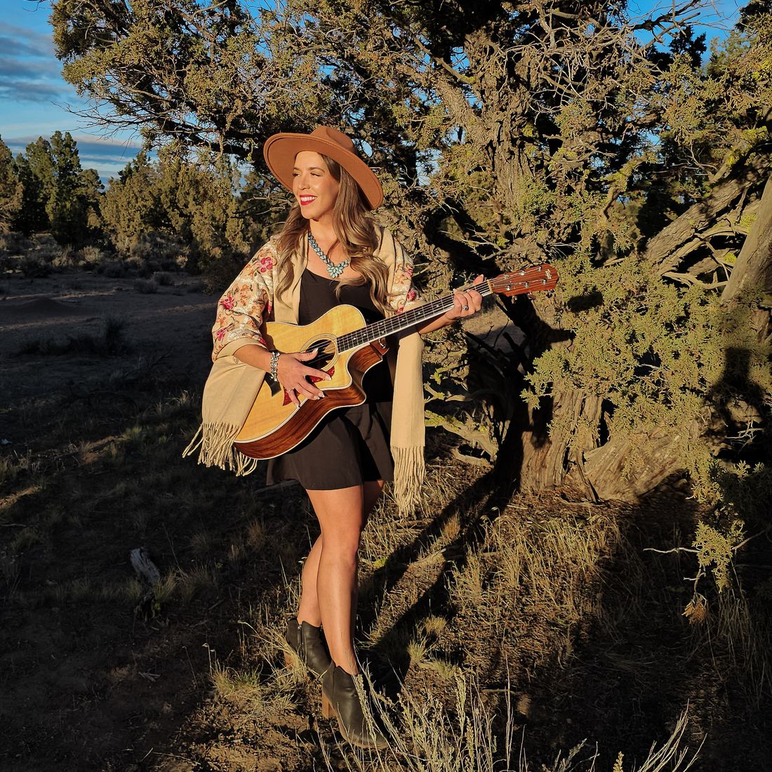 Aliki smiling with her acoustic guitar at golden hour
