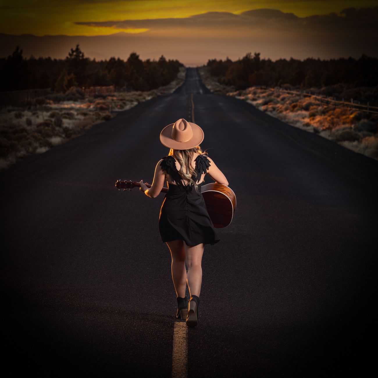 Aliki walking away down a sunset road carrying her guitar