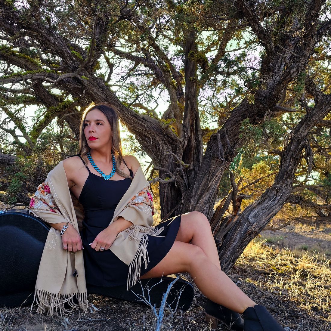 Aliki seated beneath a twisted juniper in a black dress and shawl